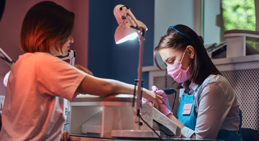 Young attractive manicurist is doing nail care for another woman