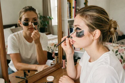 Jeune femme appliquant un maquillage d'araignée simple avec un pinceau et seulement deux produits de maquillage devant un miroir